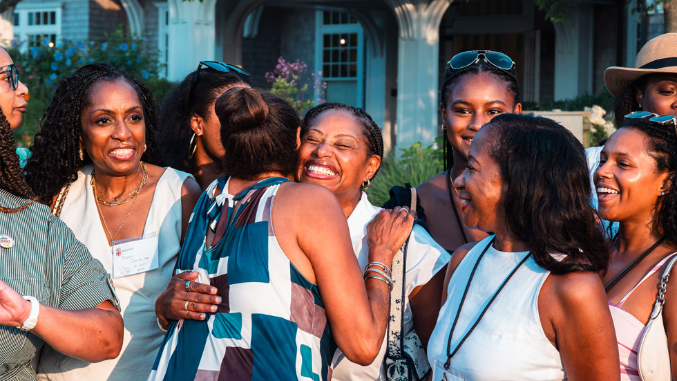 Two women embrace in a hug, as other women stand around them smiling.