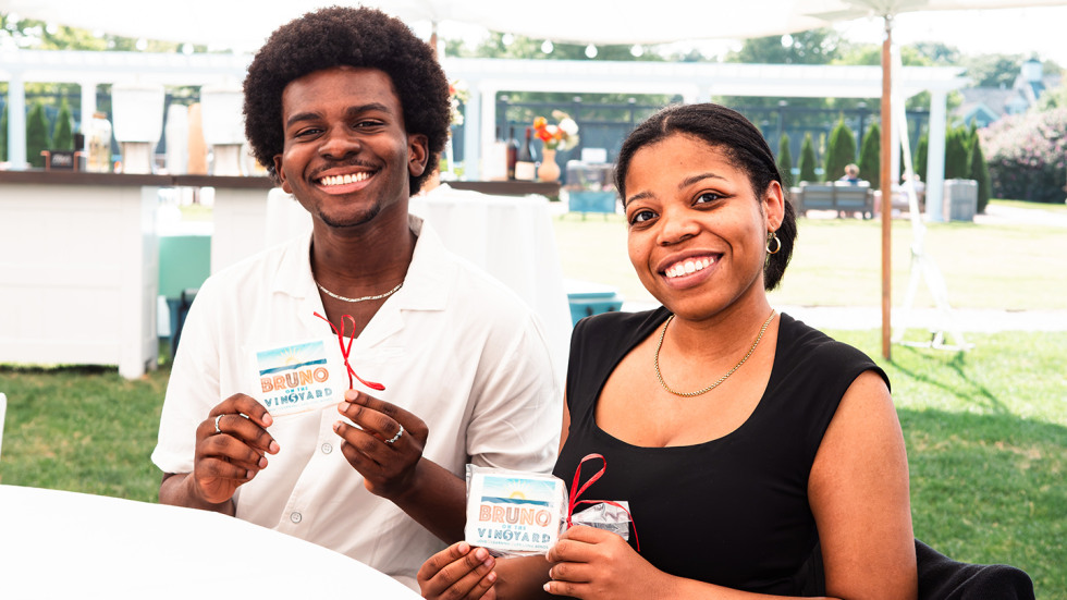 Matthew Atiogbe and Tenasica B. Barnwell seated next to each other, holding up their party favors that say Bruno on the Vineyard.