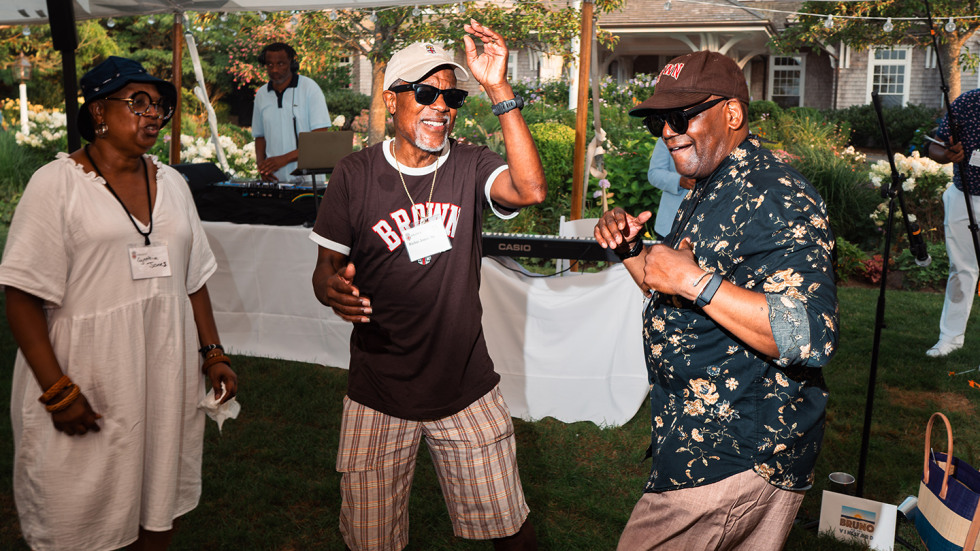 Two men and a woman are dancing on the dance floor. One man has his arm raised in the air.