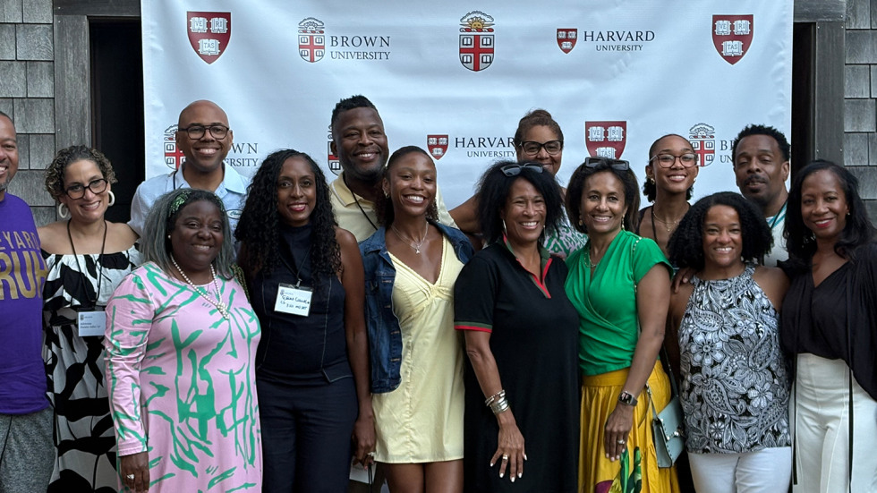 A group of alums gathered together in front of a large banner that says Brown University and Harvard University. 