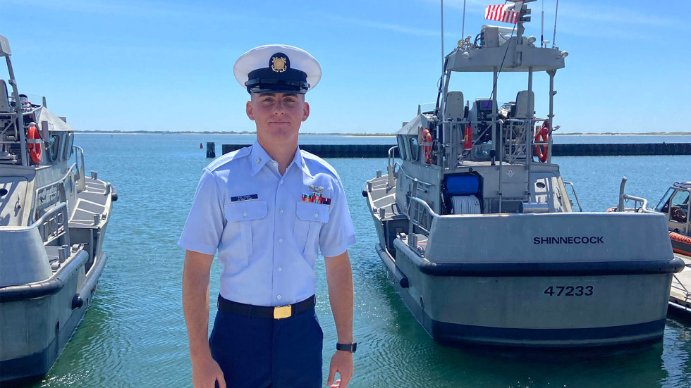Wyatt Feltner in uniform in front of a U.S. Coast Guard boat.